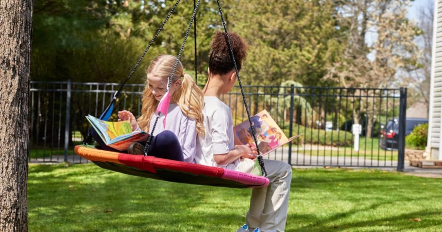 two girls sitting reading books on a saucer swing