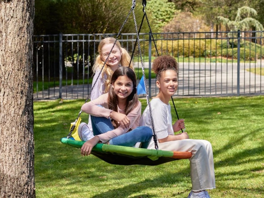 three girls sitting on saucer swing hanging from tree
