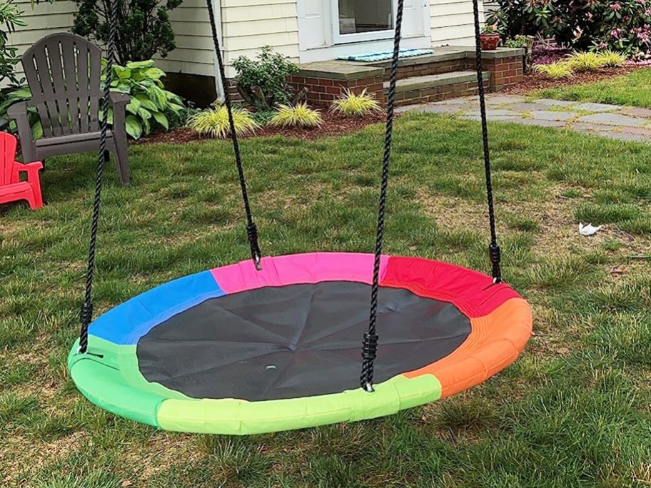 rainbow colored saucer swing hanging from tree in yard