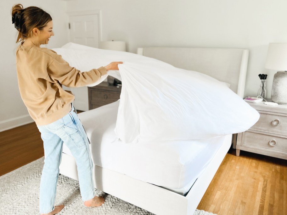 woman fluffing white sheet on bed
