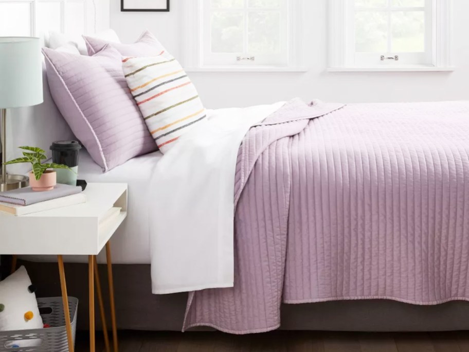 purple quilt and matching pillows on bed with white sheets