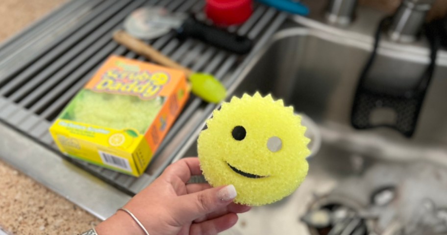 hand holding a yellow scrub daddy sponge over sink