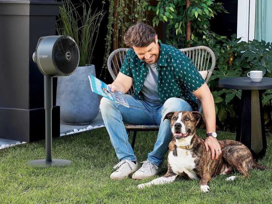 A man and his dog sitting outside next to a Shark FlexBreeze fan