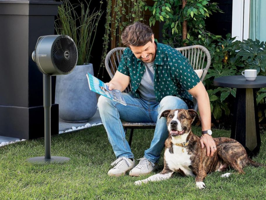 A man and his dog sitting outside next to a Shark FlexBreeze fan
