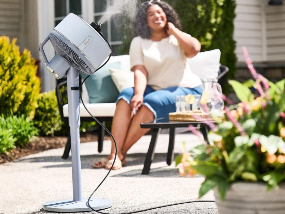 woman sitting near a Shark FlexBreeze Fan with the misting attachment in use