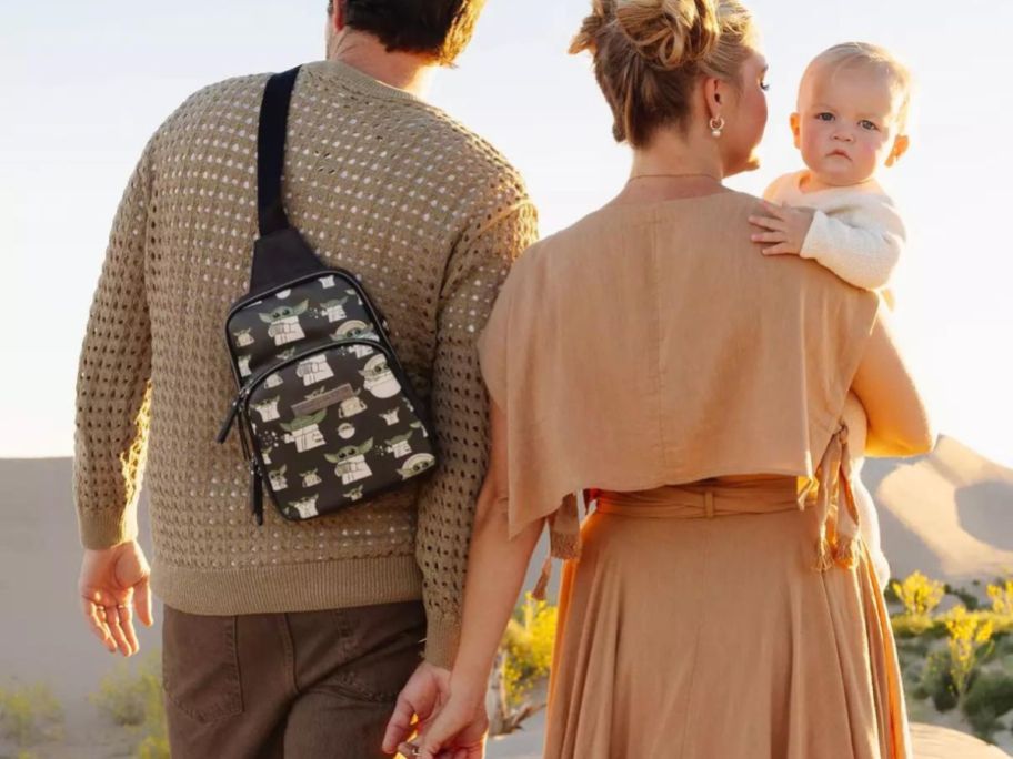 Couple with a baby and the man is wearing a Petunia Pickle Bottom Grogu Sling Bag 