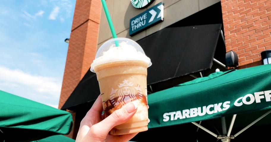 hand holding up a starbucks frappuccino outside starbucks store