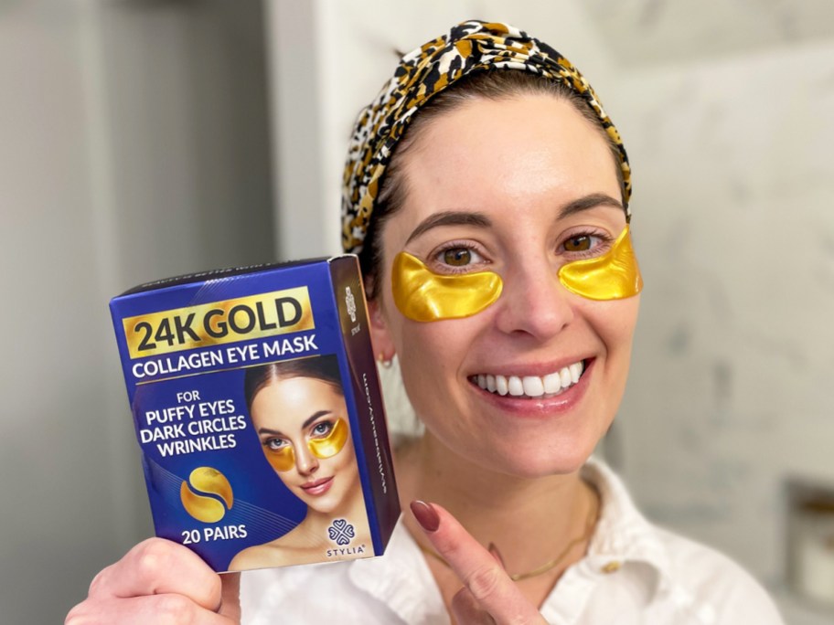woman wearing pair of gold eye masks and pointing to their box