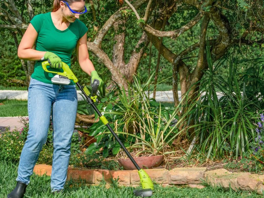woman using a Sun Joe string trimmer to trim around the edges of her yard