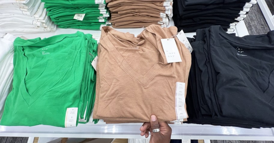 stacks of folded green, brown, and black basic tees on store display table