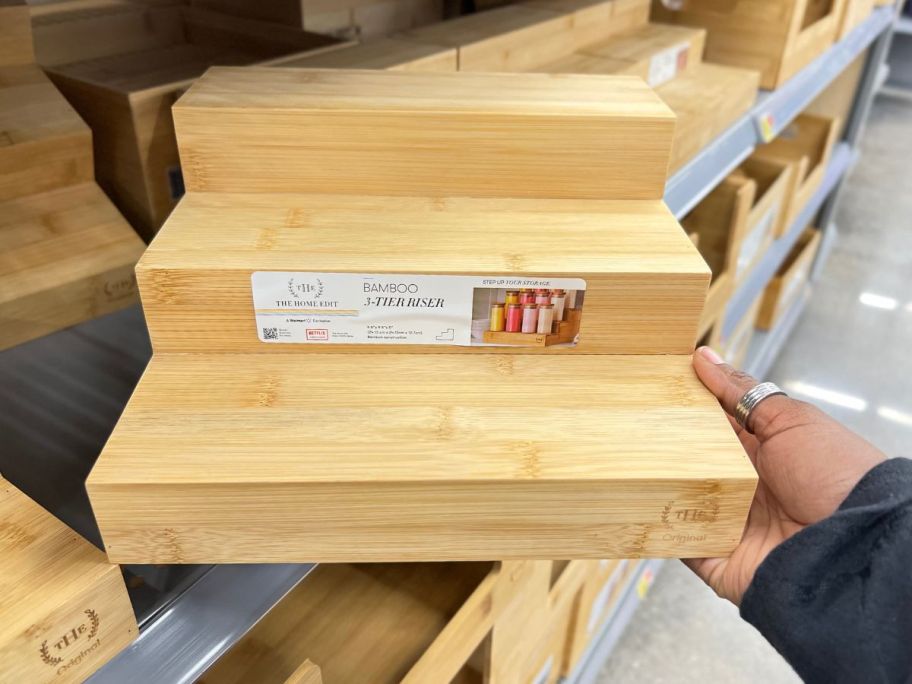 hand taking The Home Edit 3 Tier Bamboo Riser from store shelf