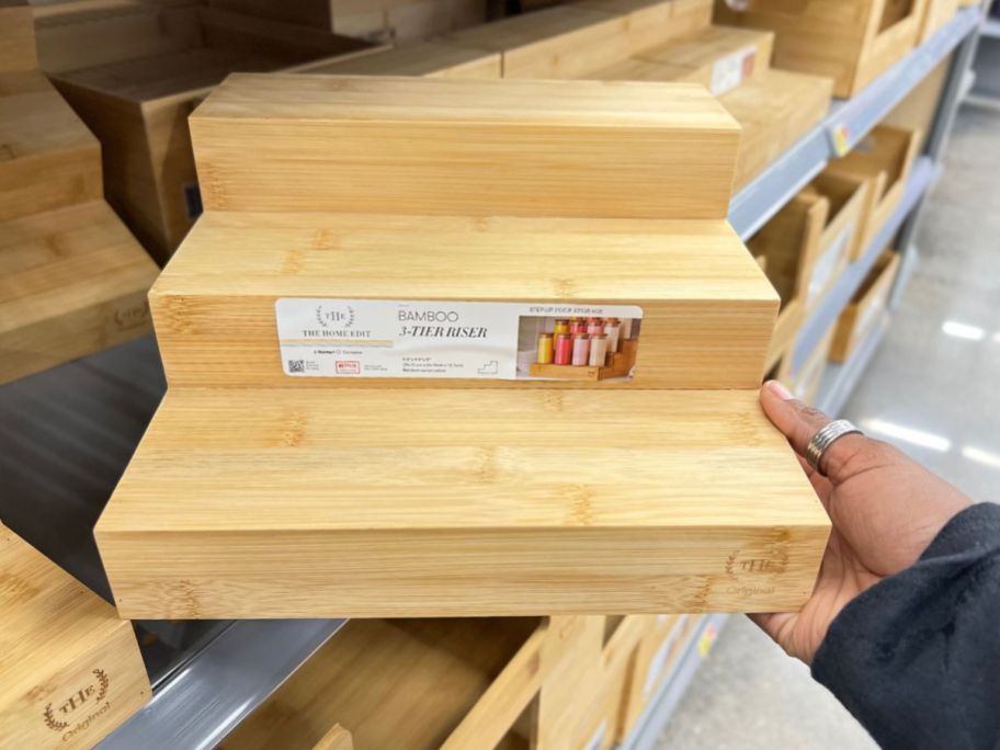 hand taking The Home Edit 3 Tier Bamboo Riser from store shelf