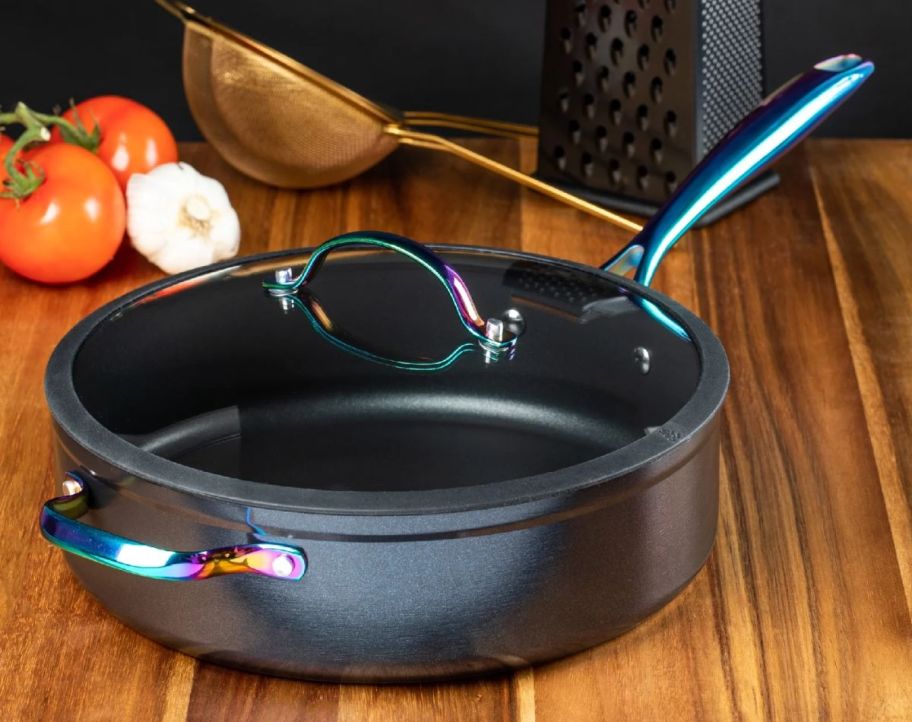 a black 5-quart non-stick saute pan with rainbow colored handles on a wooden kitchen counter