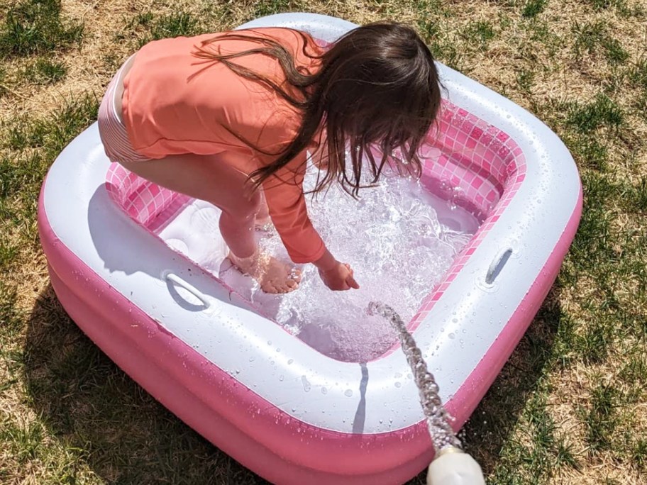 girl playing in pink and white inflatable pool on grass