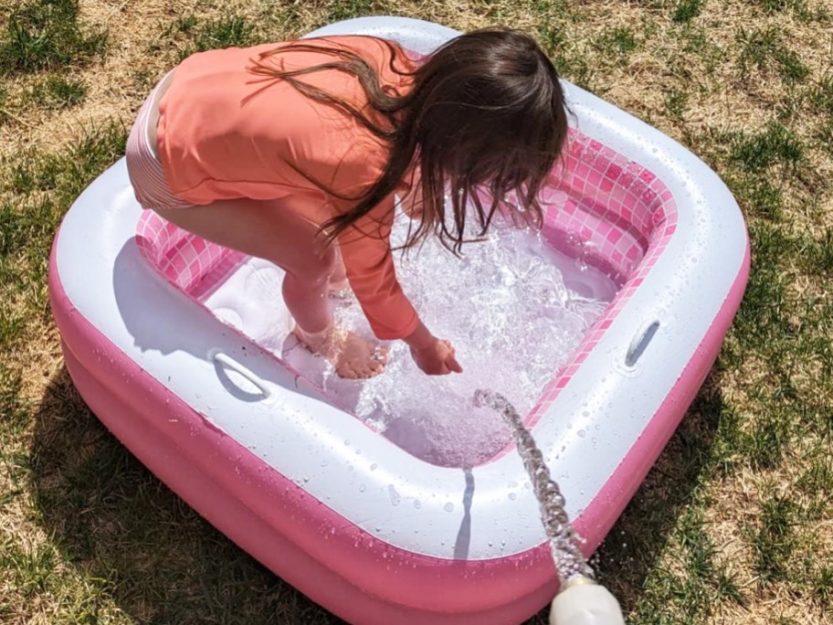 girl playing in pink and white inflatable pool on grass