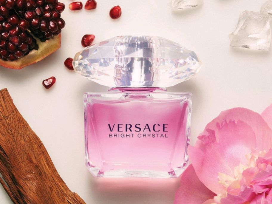 A bottle of Versace Bright Crystal perfume surrounded by ice, pomegranate, and a magnolia flower