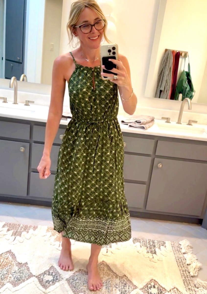 woman taking mirror selfie in bathroom wearing green dress