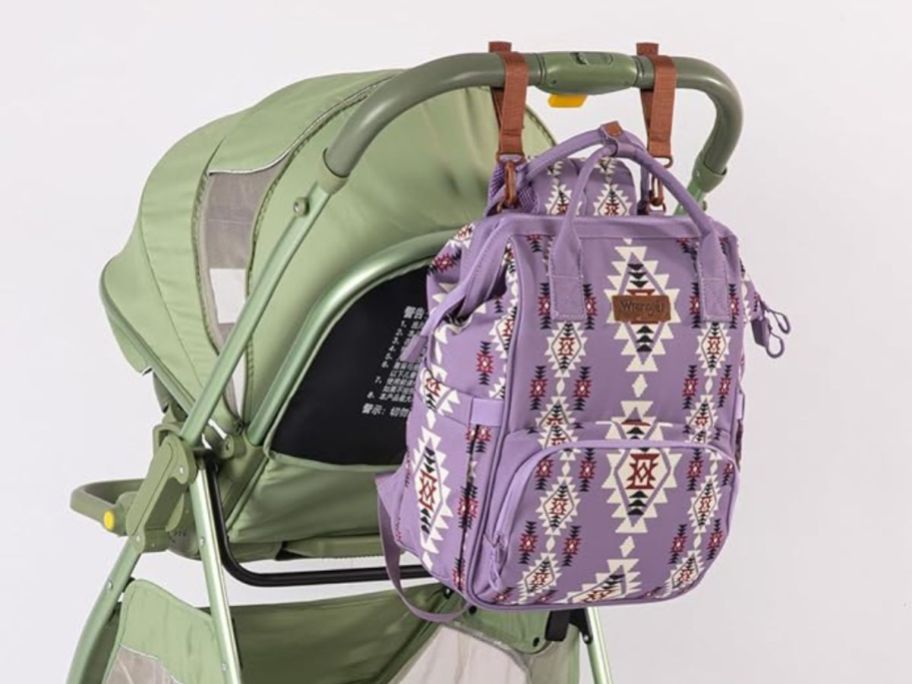 purple patterned Wrangler diaper bag backpack hanging on stroller handle