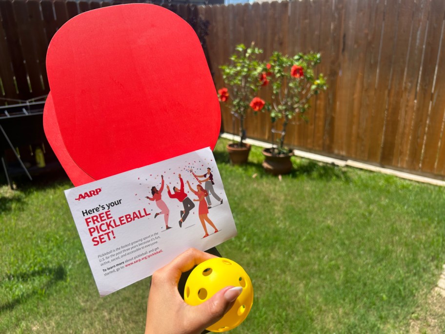 hand holding a pickleball set outside with grass in the background