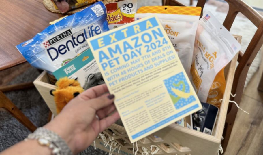 a woman holding a card about amazon pet day in front of a shipping box