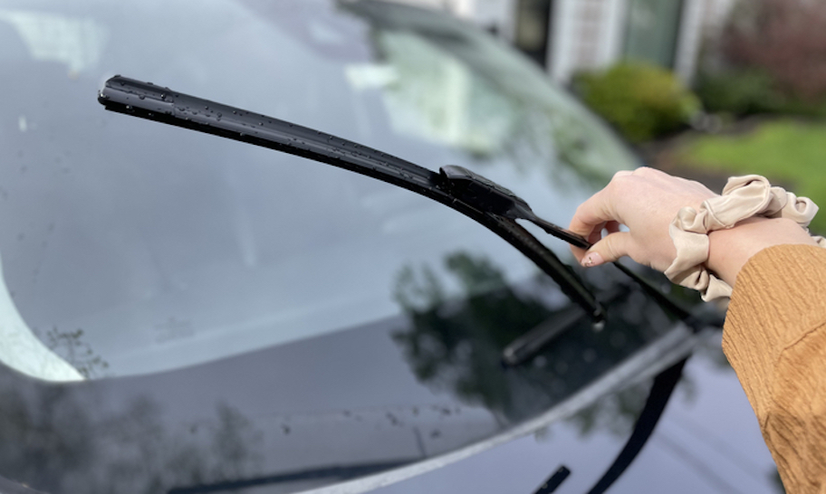 hand with scrunchie holding up windshield wiper from car