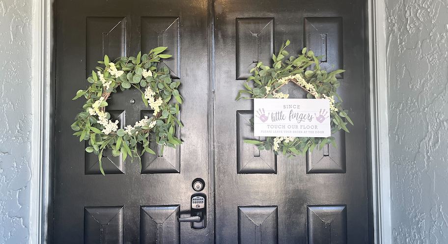 two green wreaths on front door with little fingers on floor sign