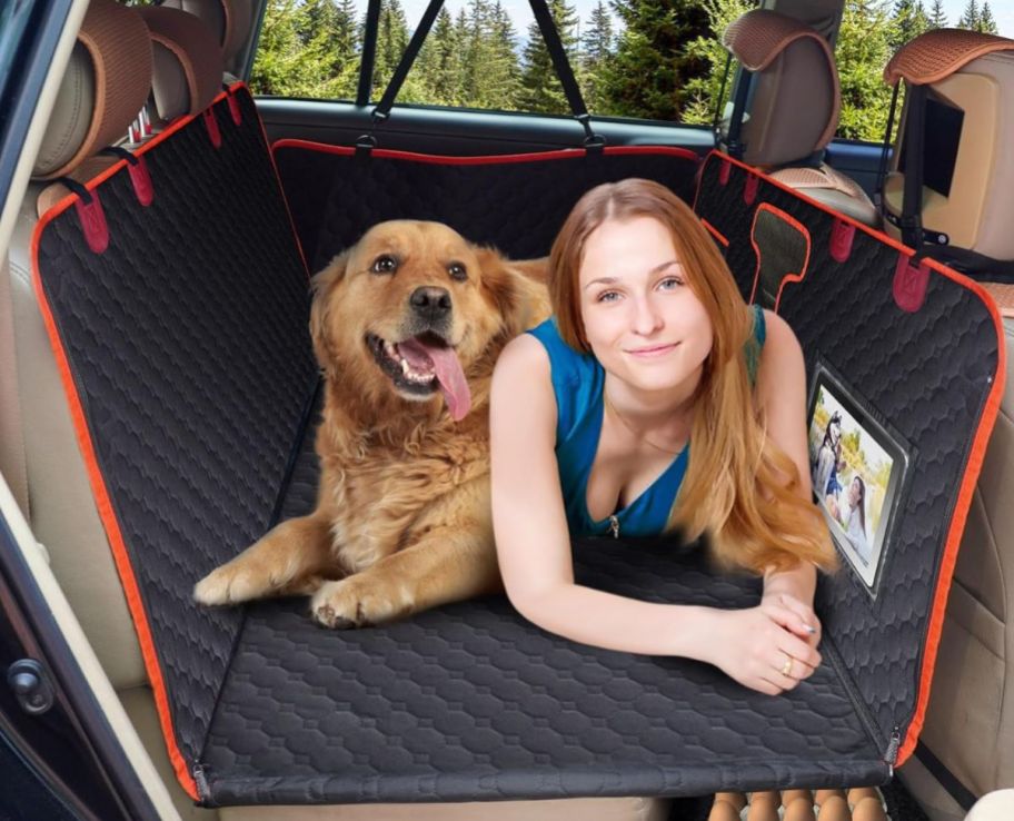 a girl and a dog in the backseat of an SUV layoing on a seat extender