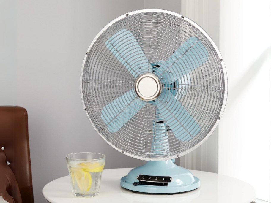light blue retro style metal table fan on a side table with a glass of lemon water