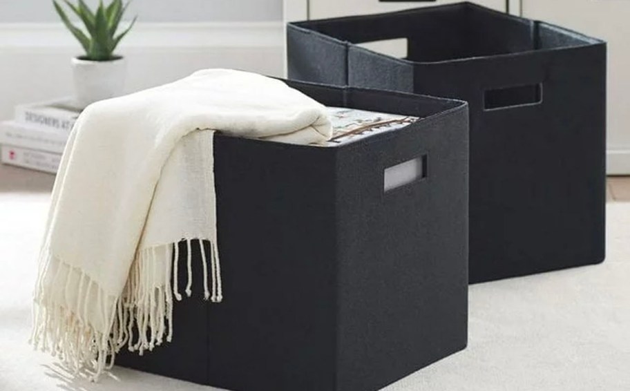 two black storage bins on carpet with white blanket laying on top