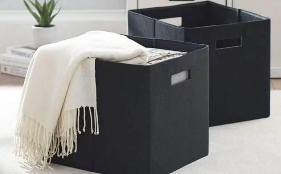 two black storage bins on carpet with white blanket laying on top