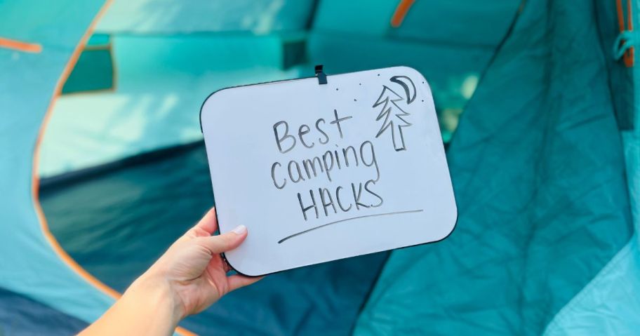 best camping hacks written on a dry-erase board held by hand in a tent