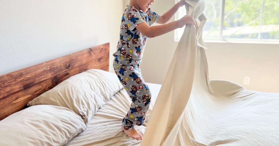 kid jumping on bed holding beige sheets