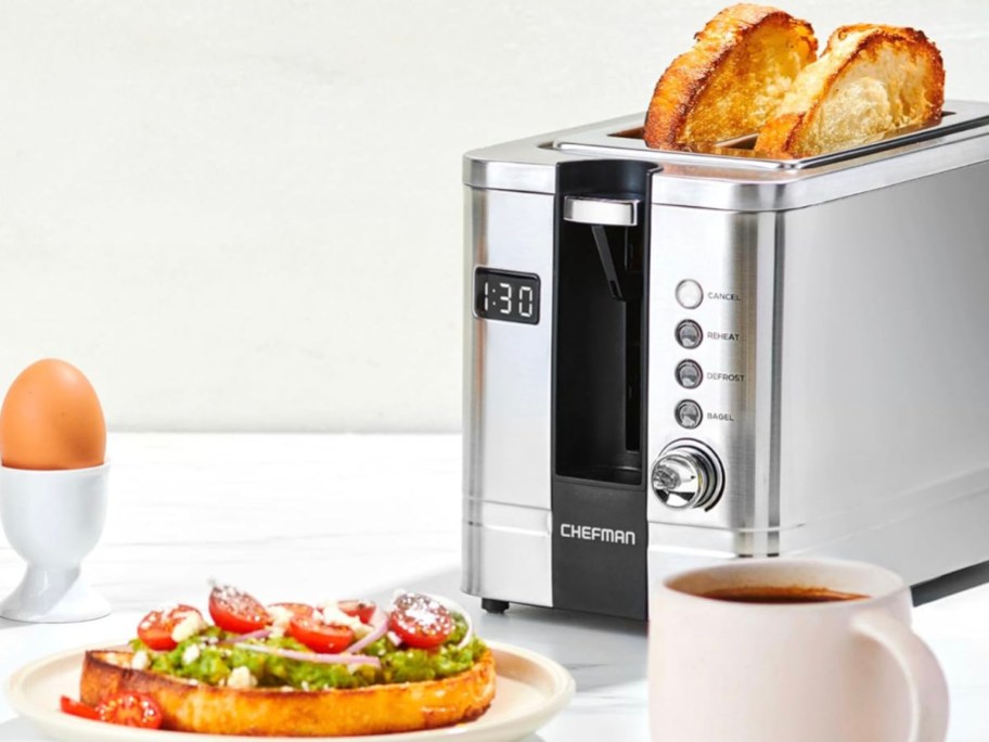 stainless steel toaster w/ bagel inside and plate with bagel and coffee cup on table