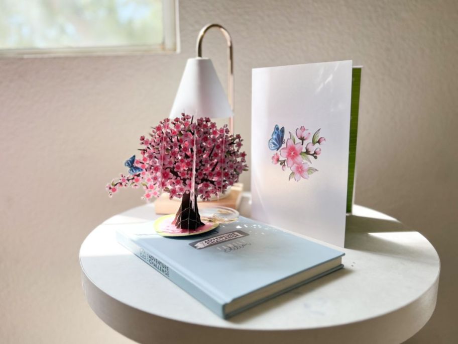 cherry blossom pop up card sits on table next to book and a lamp
