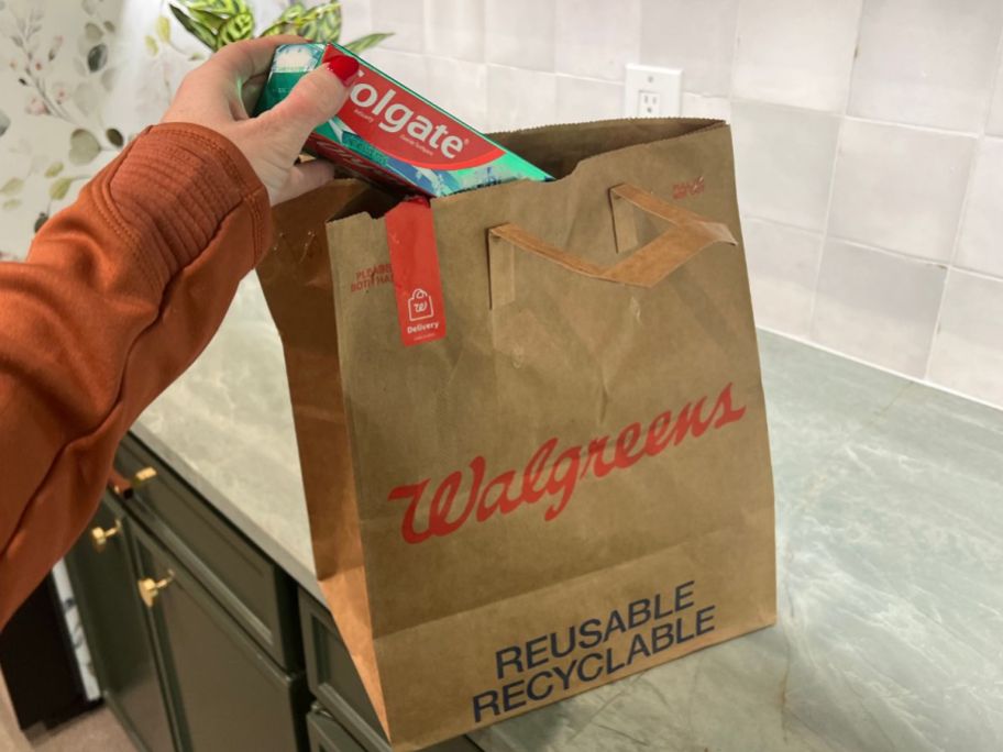 hand taking colgate toothpaste out of walgreens pickup bag
