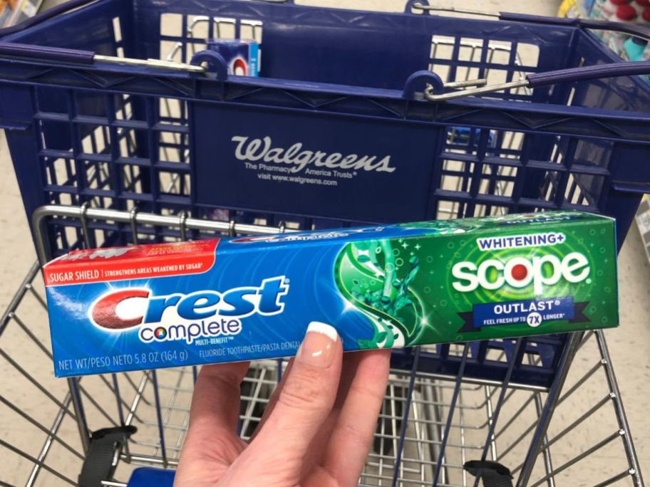 hand holding up crest toothpaste next to walgreens cart