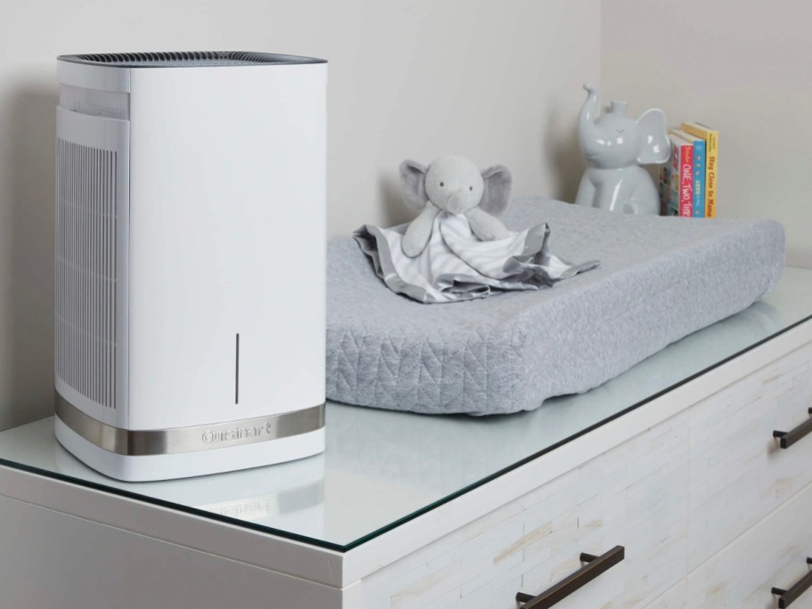 white and gray air purifier sitting on dresser with changing pad and stuffed elephant toy