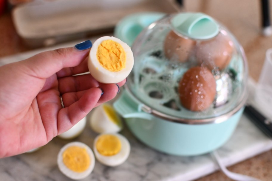 woman holding up half a hard boiled egg next to a dash egg cooker