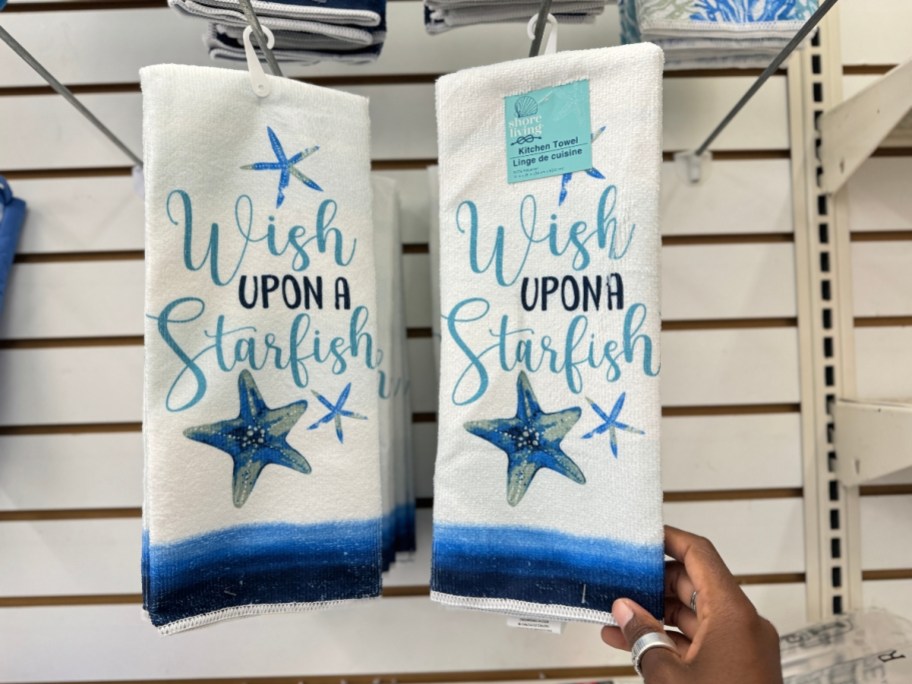 hand reaching for beach-themed kitchen towels hanging from a wall shelf