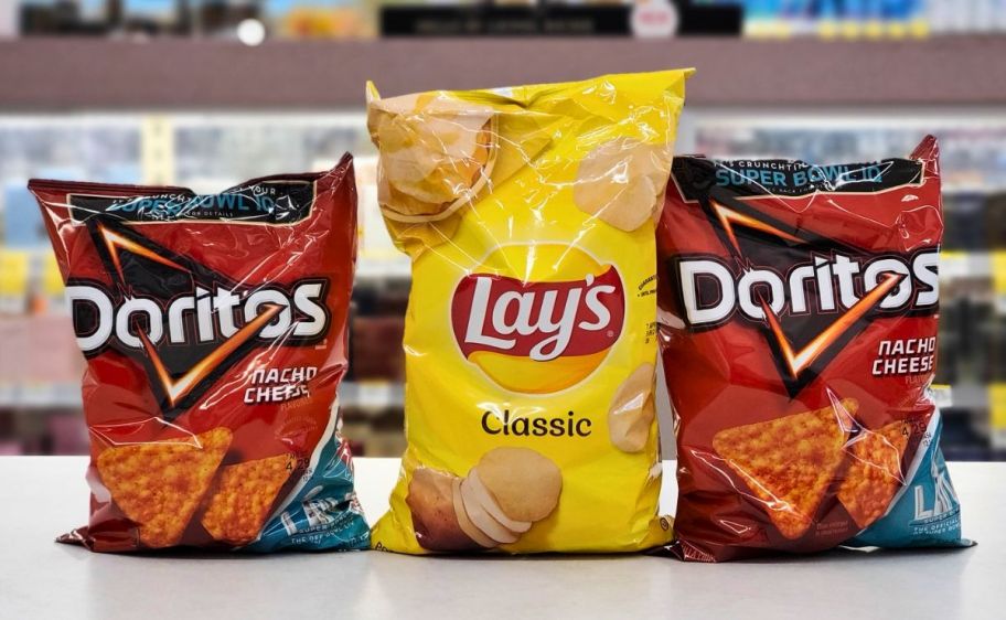 2 bags of doritos and one bag of lays potato chips on a store counter