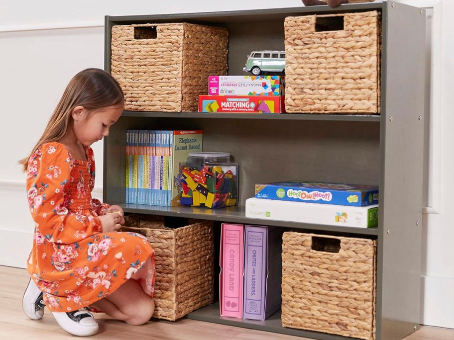 girl sitting in front of brown bookshelf with shelves and books on it. 