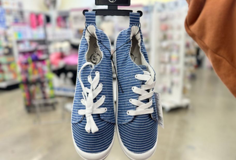 a womans hand holding a pair of blue and white striped sneakers