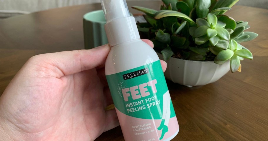 hand holding freeman foot spray bottle with plant behind it 