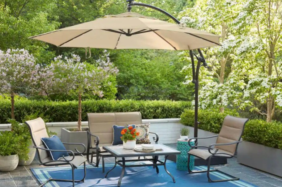tan umbrella over chairs and table on blue rug on outdoor patio