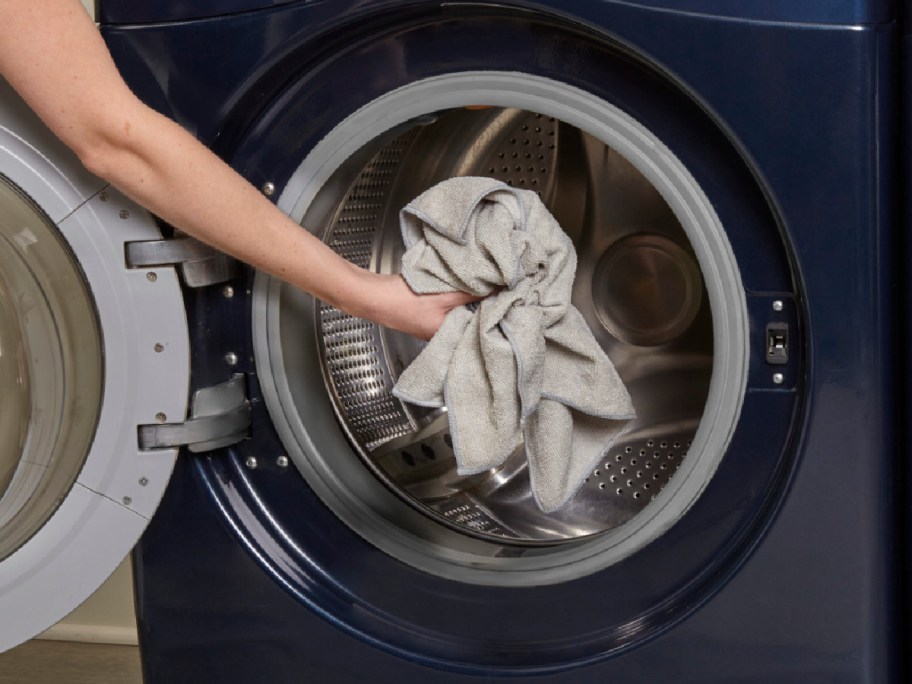 hand adding microfiber towels into washing machine