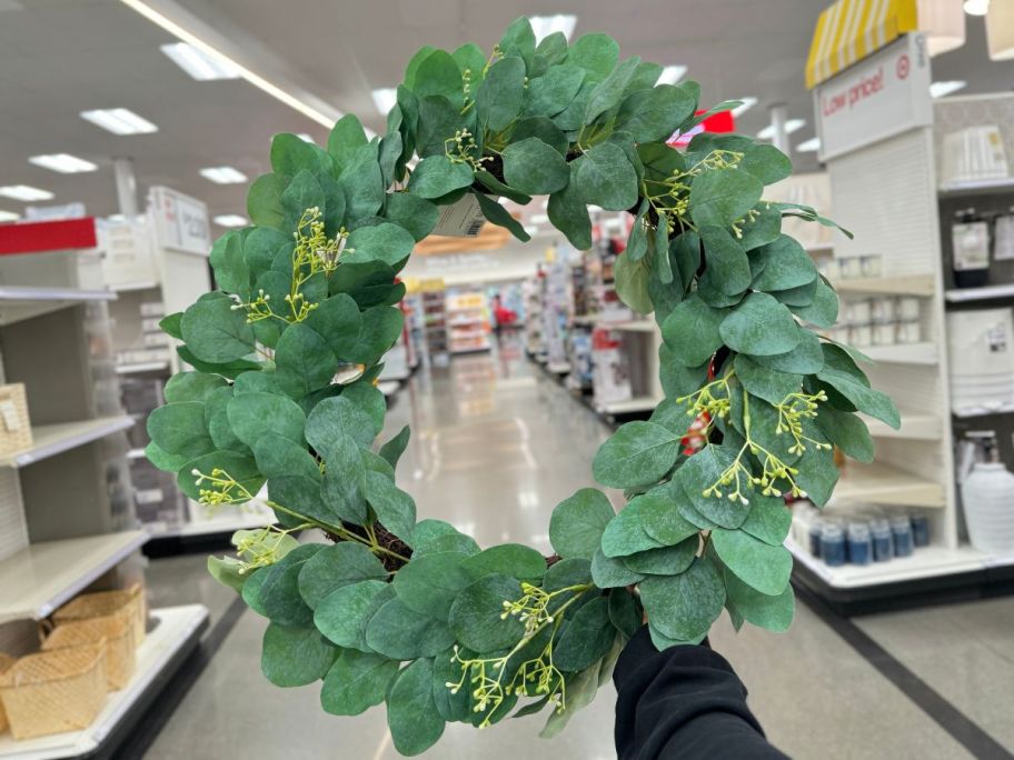 a womans hand holding a faux eucalyptus wreath on a target store aisle