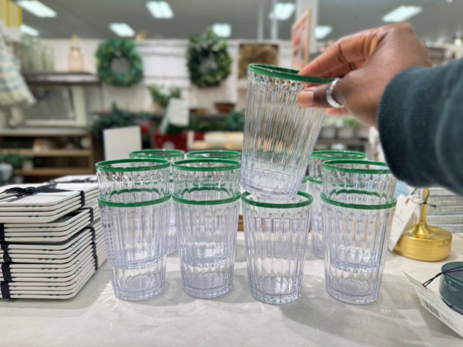 hand holding a clear with green rim tumbler with more around it