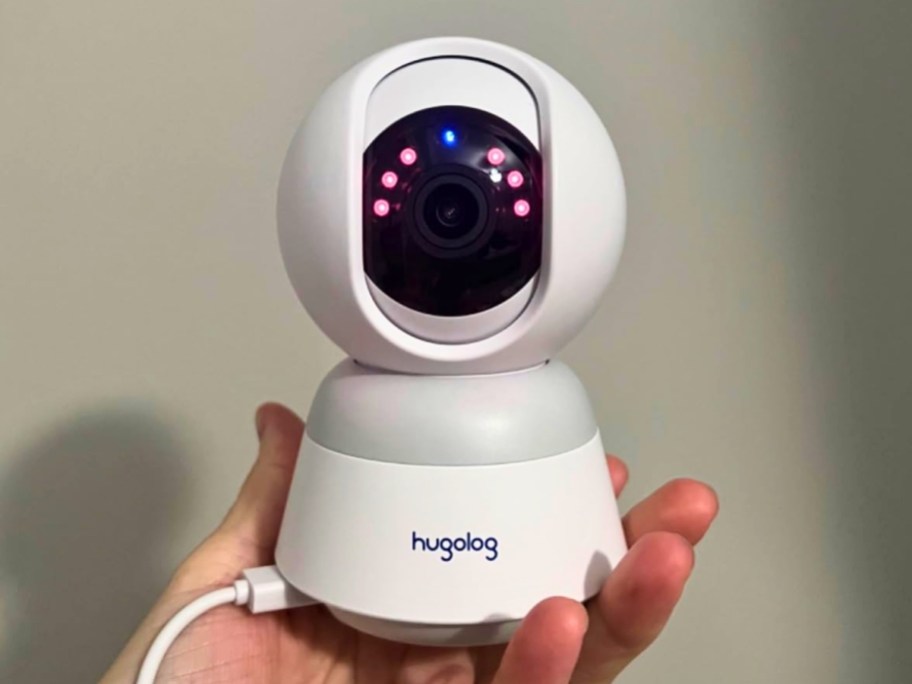 hand holding a small white indoor security camera