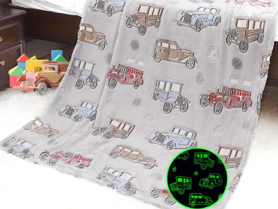 grey plush blanket hanging off a bed with vintage cars on it, toys to the side