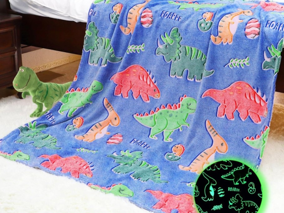 blue plush blanket with colorful dinosaurs spread out over blanket, stuffed Dino on floor beside it